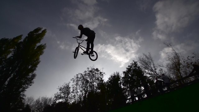 Silhouette of jumper, performing BMX mountain bike sport jump. Slow Motion 400 fps