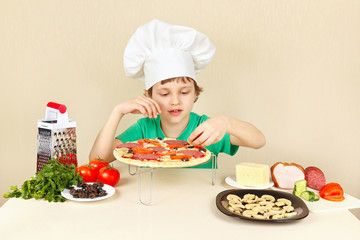 Little funny chef puts the ingredients on the pizza crust