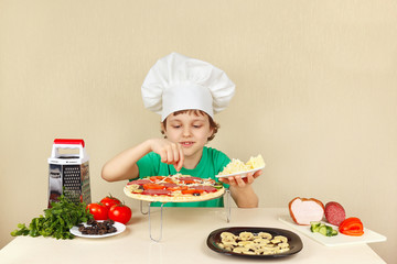 Little funny chef puts a grated cheese on the pizza crust