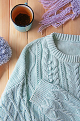 Mug of tea and warm clothes on wooden background