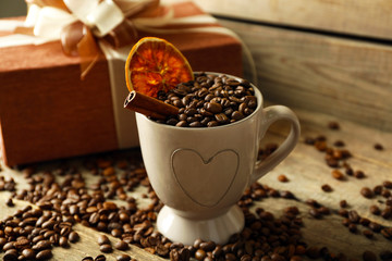 Beautiful gift with bow and coffee grains in mug, on wooden background