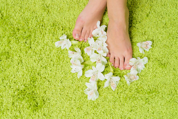 beautiful feet with pedicure and flowers at green background