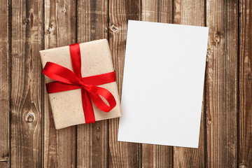 Gift box with red ribbon and blank greeting card on wooden background