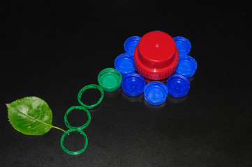 fiore creato con tappi di bottiglie di plastica e una vera foglia, sfondo scuro