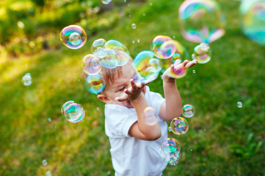 Little boy with soap bubbles in summer park.