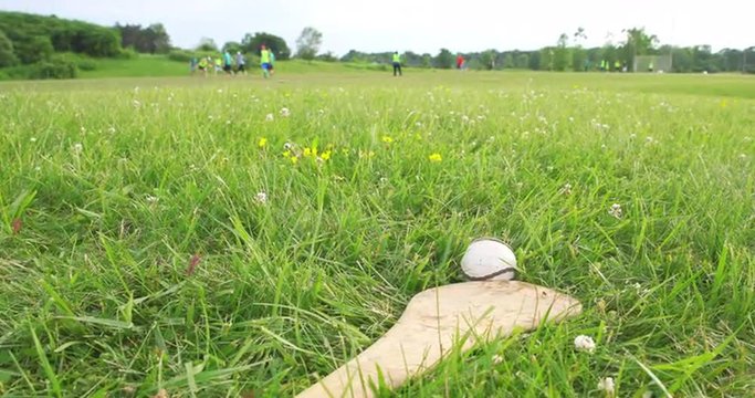 Dolly to Hurling Stick with People in Background. camera moves right to show hurley and sliota in foreground with people practicing hurling in the background out of focus
