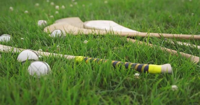 Dolly Left on Irish Hurls and Balls. camera dollies left on a group of irish hurleys and sliotars in a grass field

