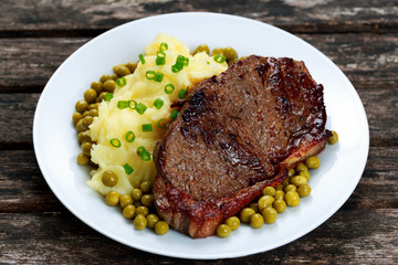 Rare beef steak with mashed potatoes, green peas