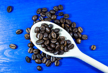 Coffee beans in wooden spoon on blue background