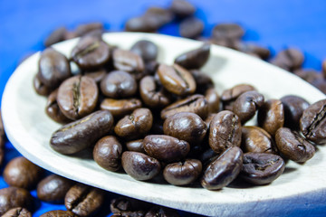 Coffee beans in wooden spoon on blue background