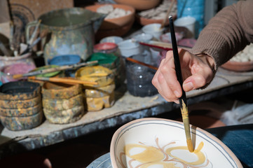 Pottery decorator from Caltagirone while finishing a ceramic tray in her work space