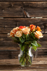 Bouquet of orange roses in vase on brown wooden background