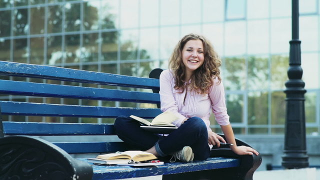 portrait of a happy female student sitting on a bench with books slow motion