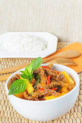 Thai red curry with beef and pumpkin in a white bowl, served with wooden spoon and fork (focus on curry)