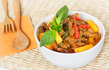 Thai red curry with beef and pumpkin in a white bowl, served with wooden spoon and fork