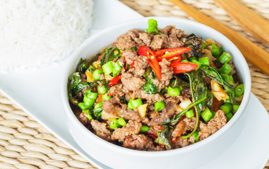 Stir fried chopped meat with chili and basil in white bowl and separated steamed rice on white plate