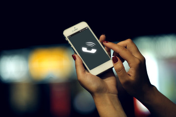 Female hand with mobile phone on blurred night lights background