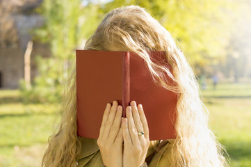 Blonde girl covering face with a book