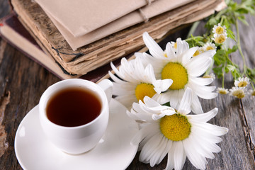 Old books with beautiful flowers and cup of tea on wooden table close up