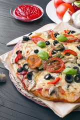 pizza with tomatoes, mushrooms, olives and peppers served on a wooden table