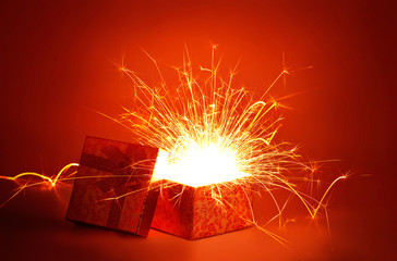 Open gold gift box and light fireworks christmas on red background