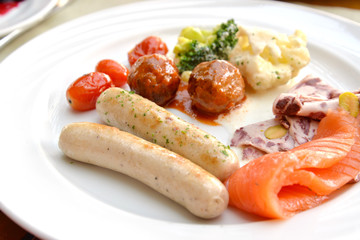Breakfast buffet with sausage, meat ball, cold cut, smoked salmon, cauliflower and tomato on white plate
