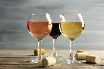 Composition of wine glasses and corks on wooden table against grey background
