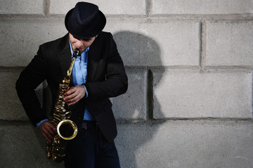 Elegant young man with sax on brick wall background