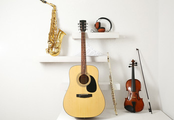 Musical instruments and headphones on decorated shelves against white wall background