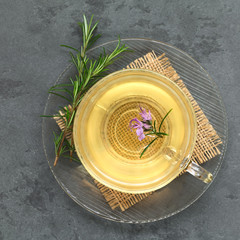 Freshly prepared rosemary herbal tea in glass cup, garnished with rosemary flower, photographed overhead on slate with natural light (Selective Focus, Focus on the top of the tea and the flower)