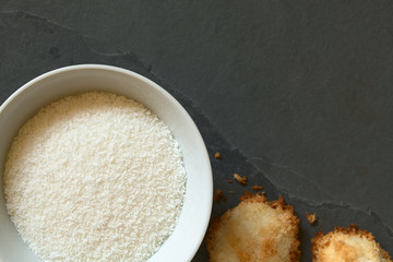 Grated coconut in bowl with coconut macaroons on slate, photographed overhead with natural light (Selective Focus, Focus on the grated coconut)
