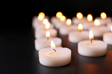 Fototapeta na wymiar Alight candles in a row on black background, blurred
