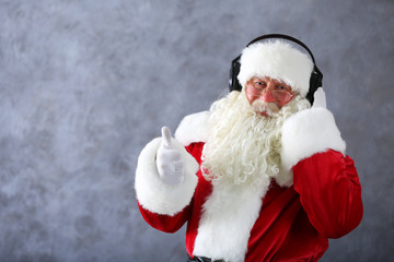 Santa Claus with headphones listening to music on gray wall background