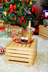 Delicious cupcakes and champagne on table, on Christmas tree background