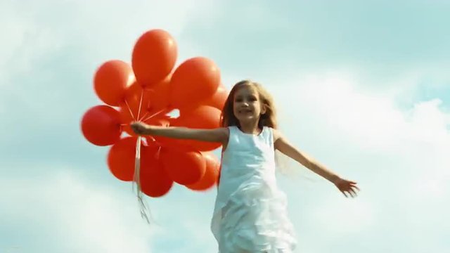 Girl in a white dress holding red balloons and spinning against the sky