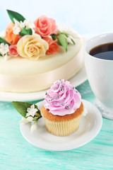 Cake with sugar paste flowers and cupcake, on light background