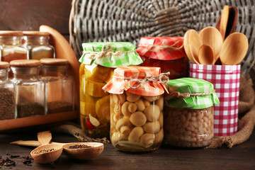 Fototapeta na wymiar Jars with pickled vegetables, beans, spices and kitchenware on wooden background