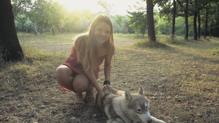 teenage girl caresses a husky dog and looks in camera in forest slow motion