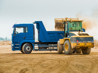 Huge backhoe loader filling the excavated soil inside blue dump truck