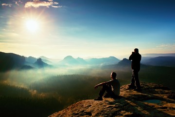 Hiker and photo enthusiast stay with tripod on cliff and thinking. Dreamy fogy landscape, blue...