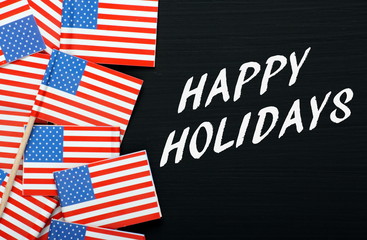 The phrase Happy Holidays in white text on a blackboard next to small flags of the United States of America