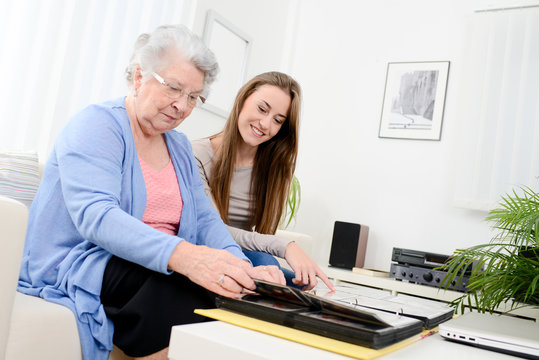 elderly woman with her young granddaughter at home looking at memory in family photo album