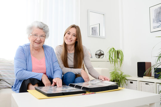 elderly woman with her young granddaughter at home looking at memory in family photo album