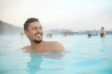Smiling hispanic young man relaxing in pool in Iceland. Happy handsome latino male person in a blue...