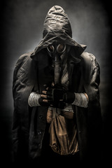 man in the gas mask in the hood, on the black background surrounded by smoke, with hands on the chest, survival soldier after apocalypse.