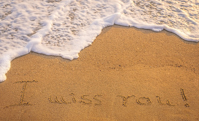 Dramatic inscription "Miss You" on wet golden beach sand in suns