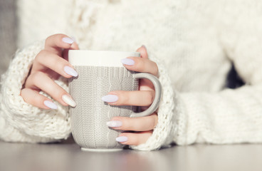Close up of woman's hands holding cup of hot coffee drink. She is wearing warm cardigan. Winter...
