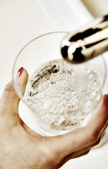 Frauenhand hält  Wasserglas unter einen Wasserhahn mit fliesendem Wasser