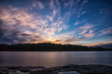 Autumn sunrise by forest lake with a blue cloudy sky with golden colors in the clouds