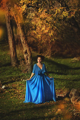 Naklejka premium young women in a blue long dress at sunset in a forest .Beautiful young woman in blue dress in garden on sunset . pretty young blonde in a teal green prom dress outdoors in a field